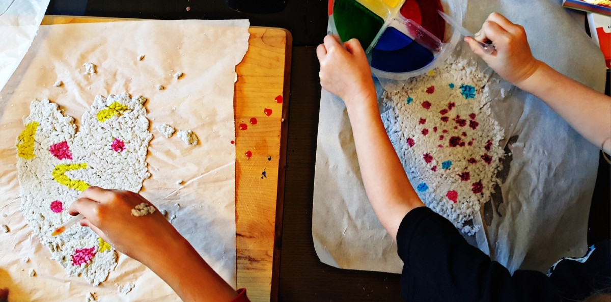 A table with hands making paper and crafts on table.